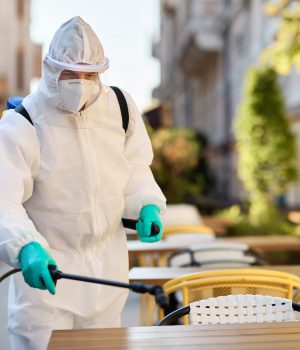 Sanitation worker in protective suit doing disinfection of an outdoor cafe due to coronavirus pandemic.